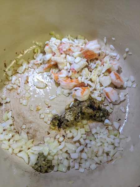 Cooking onions, Dungeness crab fat, crab meat and shrimp in a pan